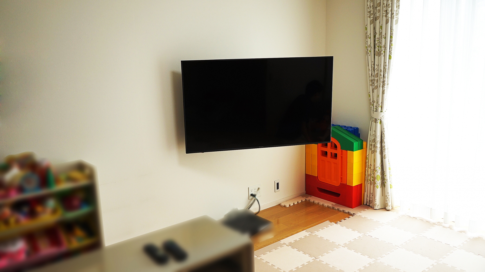 事前に補強された壁に、55インチのPanasonic・VIERA(ビエラ)「TH-55FX750」を壁掛け施工させていただきました。

オーナー様は、テレビの買い替えがキッカケとなり壁掛けテレビについて本格的に調べられたそうです。

色々と調べるうちに壁掛けテレビの見た目の美しさや、テレビを左右に振れる壁掛け金具にする事で、広いリビングの様々な所からでもじっくりと画面を見れる事を大きなメリットに感じられたと仰っていました。

壁には既に補強下地が入っているという事もあり、「壁掛け金具を購入し自分でできるのでは？と考えた」とお聞きしましたが、配線の処理に悩まれて依頼されたとお伺い致しました。

元々のテレビ用コンセントから壁掛けテレビ用に高い位置へコンセントを新設し、ブルーレイレコーダーとの接続ケーブルも全て壁内で配線させていただきました。
今まで高さのあるテレビ台を置かれていましたが、壁掛けテレビに合うオシャレなローボードタイプに替えられますね。と大変喜んで頂く事ができました。

オーナー様は壁掛け金具にもこだわられて、高い剛性と設置後の見た目に美しい質感のハイエンド金具をご指示いただいた事でテレビを左右に振った際の安定感やテレビ裏を覗き込んだ際の美しさなどに大変満足していただけました。