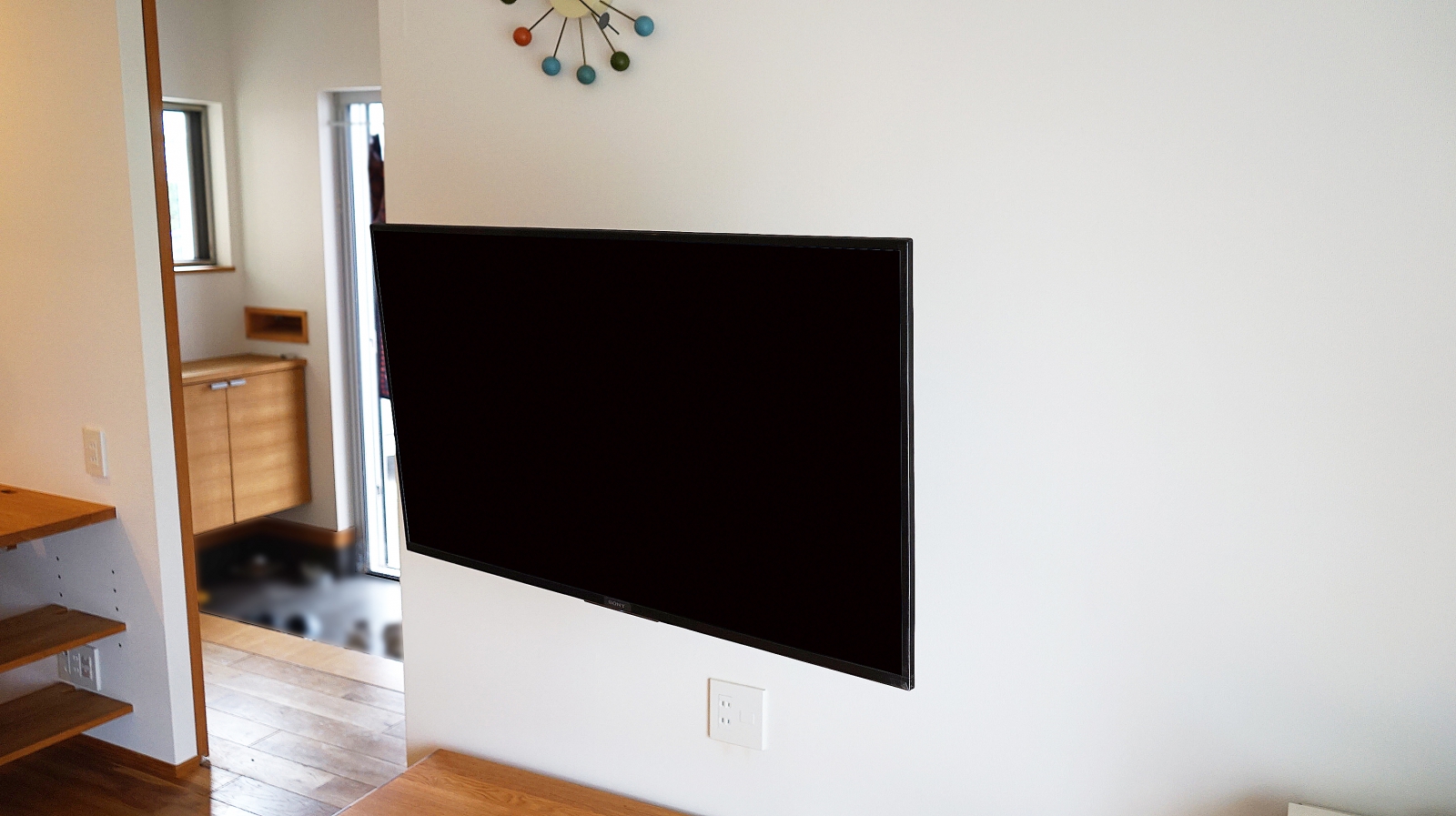 白がとても美しく明るいリビングに、43インチ・ブラビア「KJ-43X7500F」を壁掛け施工させていただきました。

壁掛け施工に合わせまして、テレビの同時購入もご用命頂きました。
ご依頼のキッカケは今まで使われていたテレビの調子が悪くなり買い替える際に、新しいテレビを壁掛けにしようと思われたそうです。

壁には補強下地があり、コンセントも通常よりも少し高い位置に設置されていました。
既存のコンセント位置は、将来的にテレビサイズが大きくなることを想定すると、壁掛けテレビ的には低い位置でしたので、そのまま残して壁掛けテレビ用に1か所新設させていただきました。

壁掛け金具には、上下左右可動式金具を用いる事で、キッチンやダイニングからの視聴にも適した角度調整が可能です。

オーナー様からは今までテレビスタンドが固定されていた為に、ダイニングやキッチンから見えにくい事も事前にご相談を受けていましたので、施工後の金具が可動した際には、イメージ以上の快適さに大変満足していただけました。

ダイニング用にもう1台壁掛け予定でしたが、可動できる金具により必要が無くなった事も大きなメリットになり、とても喜んで頂く事ができました。
