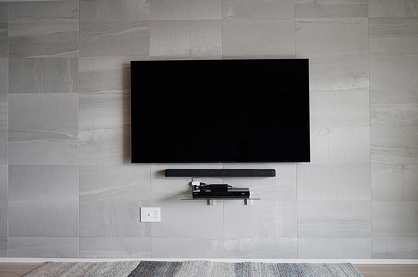 エコカラット「ストーングレース」が施された壁にソニーの有機ELテレビ65インチ「KJ-65A8F」を壁掛けさせていただきました。
エコカラット貼り付け前にジャストップ補強を施させていただき、エコカラット貼り付け後に再度訪問致しまして壁掛け施工をさせていただきました。(計2回訪問です。)
事前に補強工事をさせていただける事で、エコカラットへの開口跡もなくなり補強されていない壁でも後付け感のない美しい仕上がりになるのが魅力です。

オーナー様はさらにこだわられてサウンドバーの壁掛けとブルーレイレコーダー用シェルフの壁掛け施工も合わせてご用命いただけました。

全てをエコカラット施工の前から準備することで、エコカラットへの傷も無く美しく仕上げさせていただきました。

見た目、迫力、使い勝手においてオーナー様には大変喜んでいただけました。

弊社でエコカラットと壁掛けテレビの同時施工をご用命の際には1回のご訪問で同様な施工イメージを最短即日でご対応させていただいております。