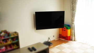 事前に補強された壁に、55インチのPanasonic・VIERA(ビエラ)「TH-55FX750」を壁掛け施工させていただきました。

オーナー様は、テレビの買い替えがキッカケとなり壁掛けテレビについて本格的に調べられたそうです。

色々と調べるうちに壁掛けテレビの見た目の美しさや、テレビを左右に振れる壁掛け金具にする事で、広いリビングの様々な所からでもじっくりと画面を見れる事を大きなメリットに感じられたと仰っていました。

壁には既に補強下地が入っているという事もあり、「壁掛け金具を購入し自分でできるのでは？と考えた」とお聞きしましたが、配線の処理に悩まれて依頼されたとお伺い致しました。

元々のテレビ用コンセントから壁掛けテレビ用に高い位置へコンセントを新設し、ブルーレイレコーダーとの接続ケーブルも全て壁内で配線させていただきました。
今まで高さのあるテレビ台を置かれていましたが、壁掛けテレビに合うオシャレなローボードタイプに替えられますね。と大変喜んで頂く事ができました。

オーナー様は壁掛け金具にもこだわられて、高い剛性と設置後の見た目に美しい質感のハイエンド金具をご指示いただいた事でテレビを左右に振った際の安定感やテレビ裏を覗き込んだ際の美しさなどに大変満足していただけました。
