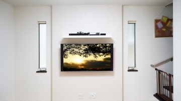 リビングのふかし壁に49インチ・液晶テレビ「TH-49EX850」と周辺機器専用シェルフの壁掛け施工をさせていただきました。

「ふかし壁はデザイン性にも美しく、オシャレな壁面を演出できる点にもこだわりました」とオーナー様よりお伺い致しました。
将来的には壁掛けテレビでよりこだわりの空間を構想されていて、補強下地も施工済みでしたので、「今回ようやく念願叶いました」と仰っておられました。

キッカケとして大きかった事は、テレビ台を無くす事による掃除のしやすさ、お子さんが大きくなる中でテレビ台に置いたテレビの転倒(接触や地震による)が心配になった事だとお聞きしました。

シェルフ位置もお子さんの手の届かない場所をイメージされてテレビ上側にこだわられた事で、テレビ下スペースをとてもスッキリとすることが出来ました。
掃除機の掛けやすさは大幅に向上し、お子さんの遊べるスペースも増えた事にも大変喜んで頂く事ができました。

壁掛け金具には、キッチン・ダイニング・リビングのどこからでも楽々視聴できるように上下左右可動式金具をご選択されました。

今回のテレビは両側にスピーカーを搭載し、テレビ背面形状が特徴的なモデルでしたので、オーナー様からは壁掛け金具についても事前にご相談を受けておりましたが、過去にも施工経験がございますので、将来的にテレビを買い替えられた際にも引き続きお使い頂ける金具をご選定させていただきました。

構想されていた壁掛けテレビの実現と合わせて、シェルフや金具のイメージ以上の使い勝手の良さにオーナー様には大変満足していただけました。
