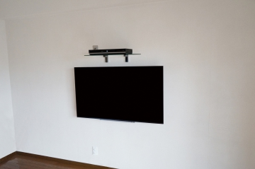 出来る限りの省スペースを意識されて、ブルーレイ用シェルフの取付と壁掛けテレビを同時施工させていただきました。
専用シェルフは、ブルーレイを少ないスペースで確保でき、壁掛けテレビをよりスッキリとした印象に引き立たせるアイテムとして人気があります。
オーナー様には弊社のシェルフ取付の施工事例を多く見ていただきご依頼されたとお伺い致しました。
お子様の手の届かない高さをイメージされてテレビ上へのレイアウトも増えています。
想像以上のスッキリとした印象にオーナー様には大変喜んでいただけました。